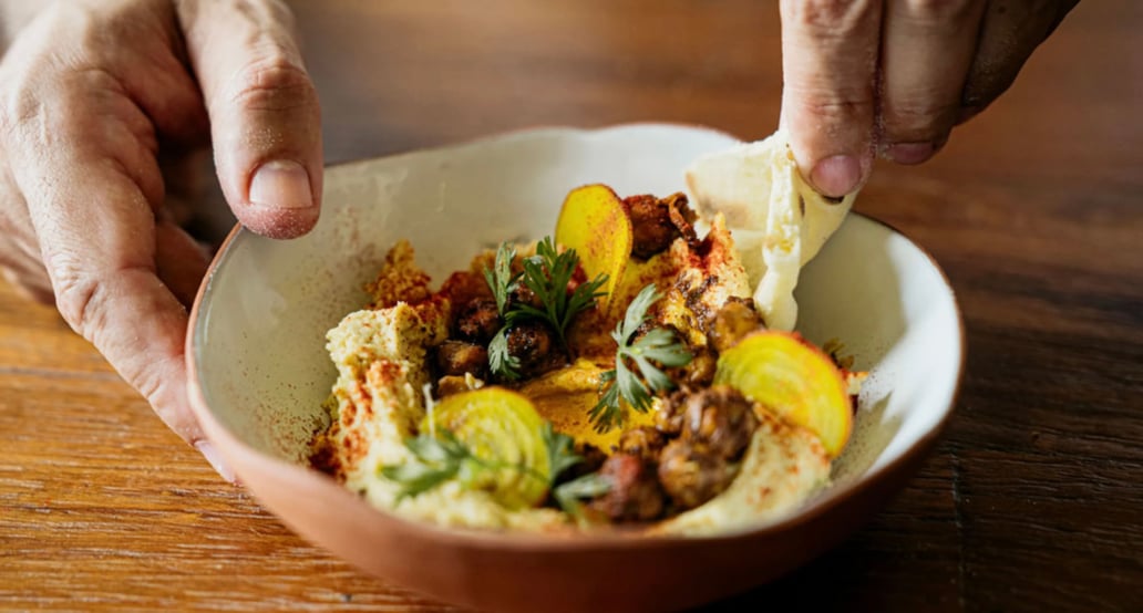 1032x554 Rosewood Mayakoba Zapote Bar_hummus dish being scooped with pita in orange bowl_WIDE-LARGE-16-9