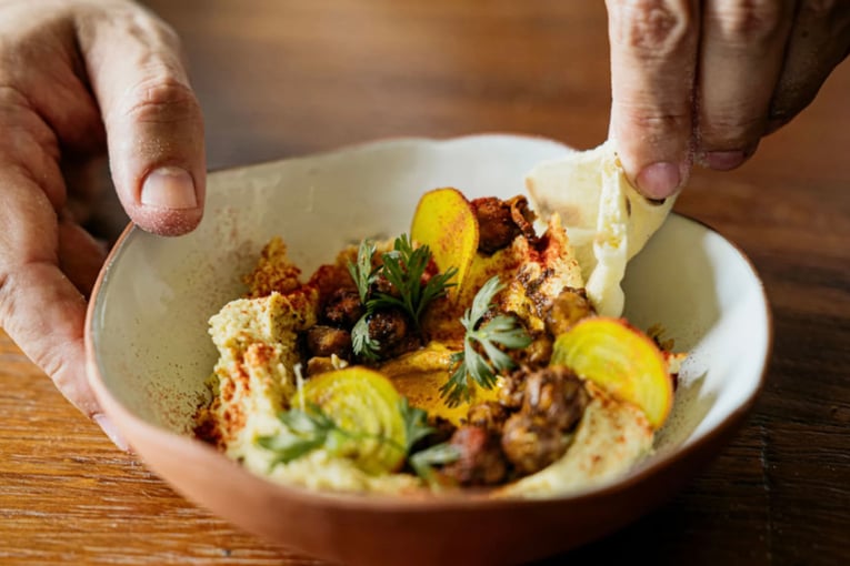 Rosewood Mayakoba Zapote Bar_hummus dish being scooped with pita in orange bowl_WIDE-LARGE-16-9